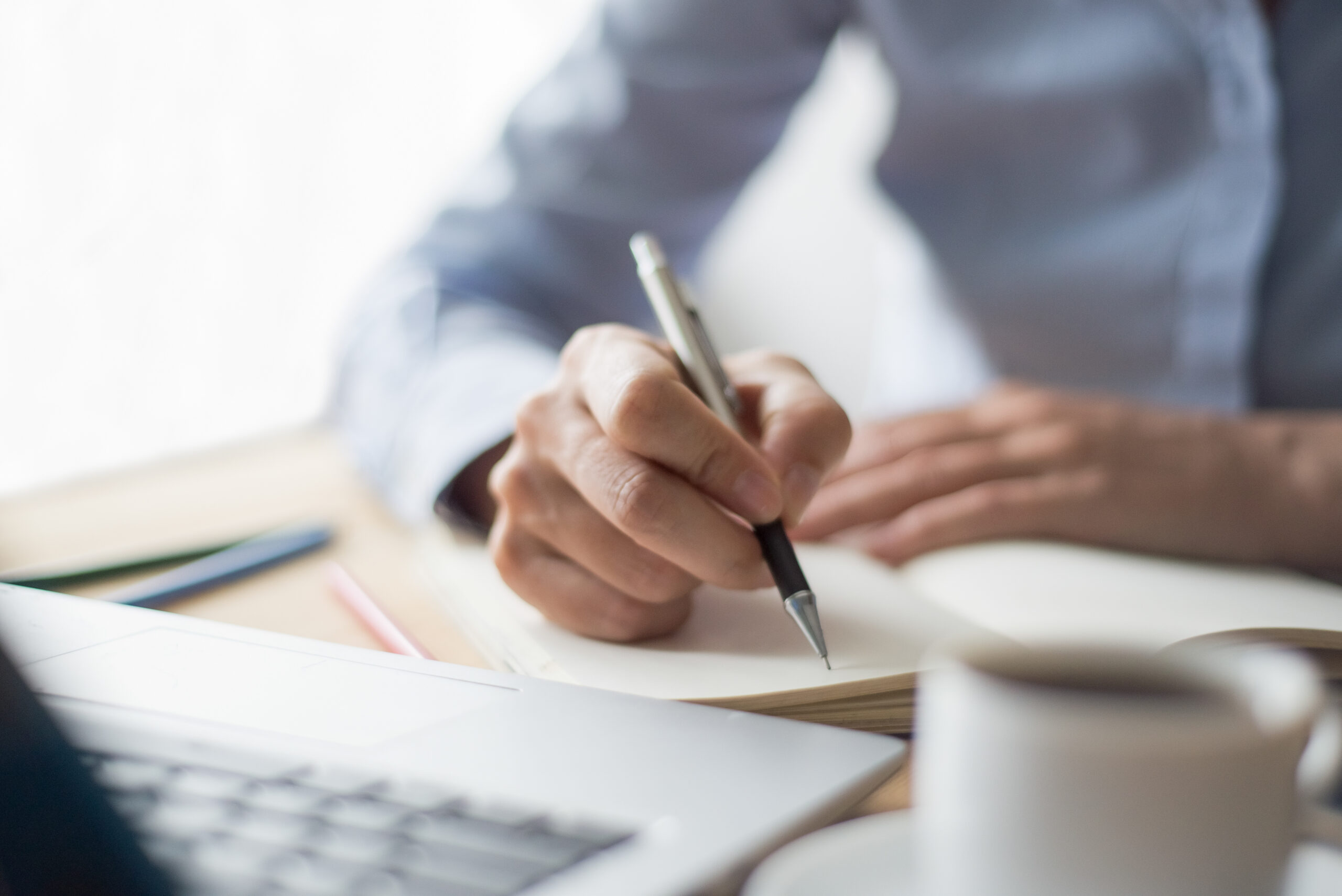 Cropped view of woman writing in notebook and sitting at desk with laptop computer