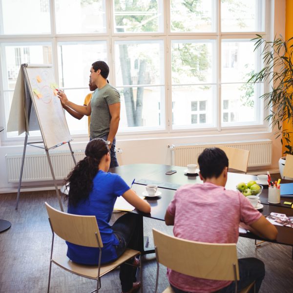 Business executives discussing with their colleagues on whiteboard during meeting at office